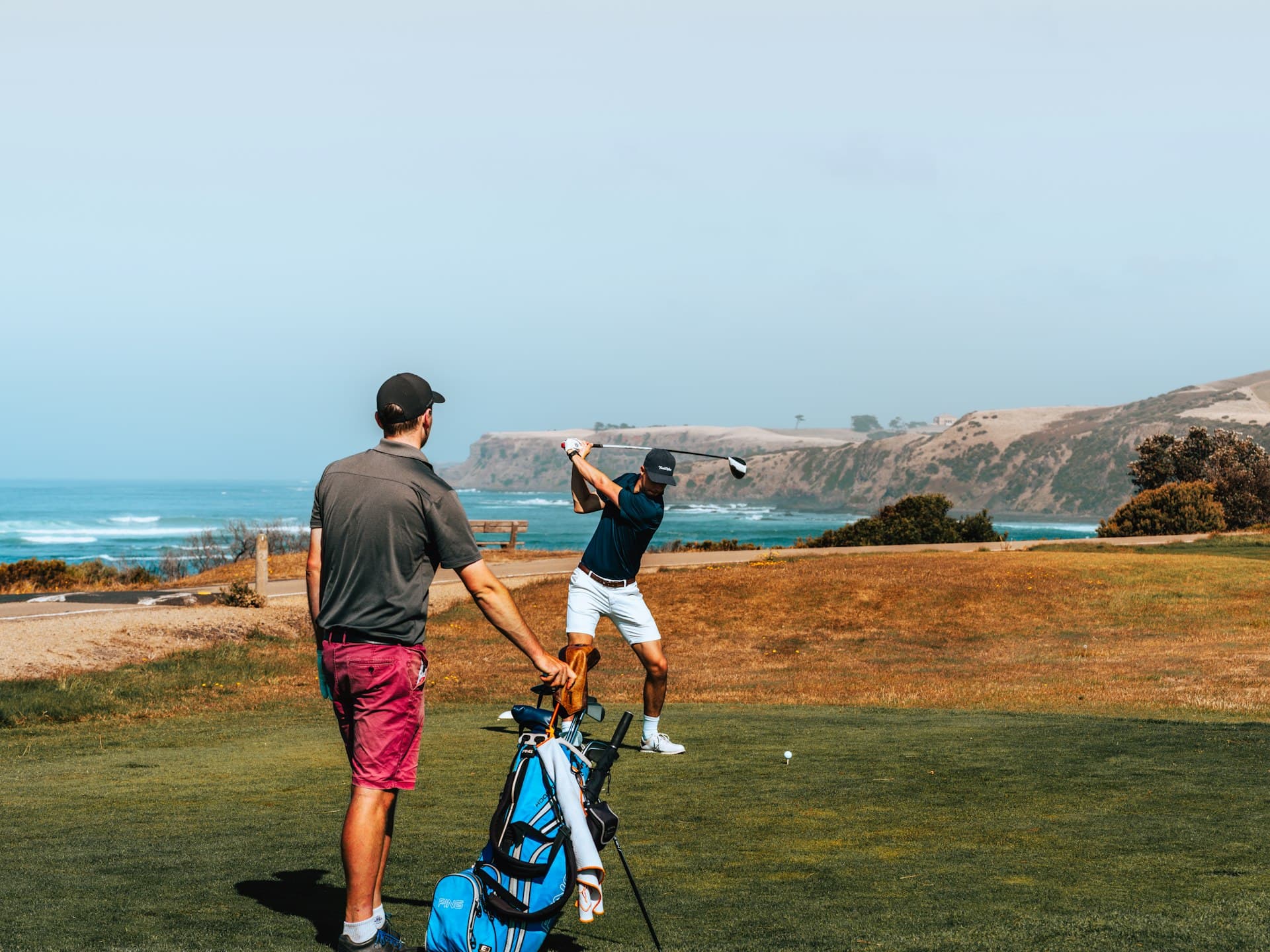 A caddy carrying the bag while a golfer tees off